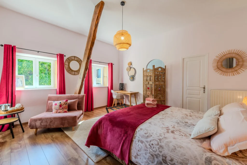 Lit au plaid bordeaux, fauteuil rose et suspension en rotin dans la chambre Prunus